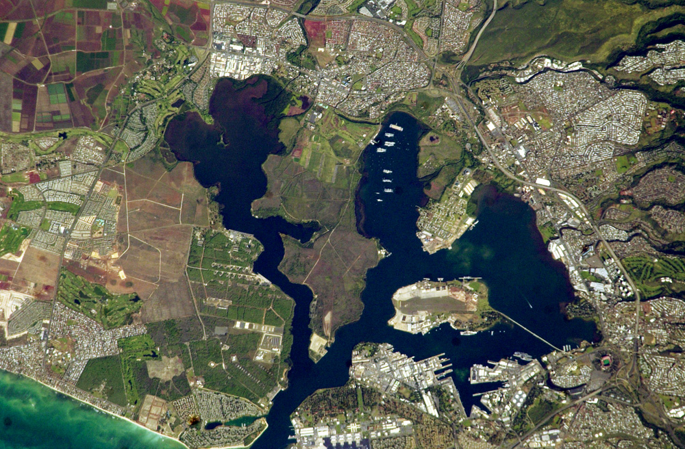 A satellite image of a blue harbor surrounded by roads and human development (NASA). 