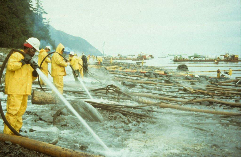 A line of clean-up workers hose off oil from a rocky shore using hot water following the Exxon Valdez oil spill. Photograph credit: Exxon Valdez Oil Spill Trustee Council