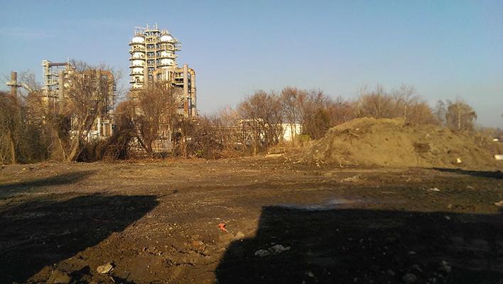 Metro Corporation industrial site cleared in the foreground with dirt piles and refinery structures in the background. 