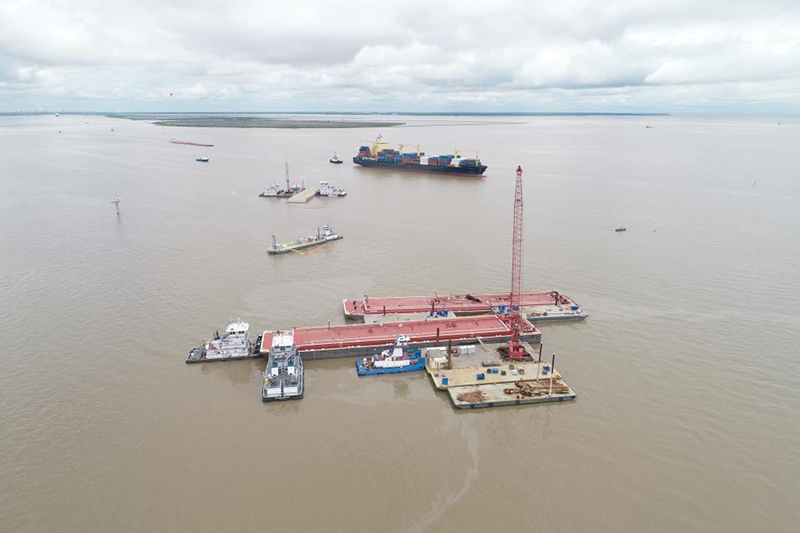 A overflight photo of vessels surrounding damaged barges in brown water. 