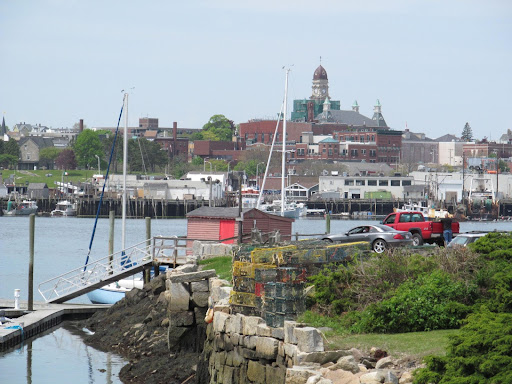 the Gloucester harbor is pictured with boats in the background and a small boathouse and ramp in the foreground