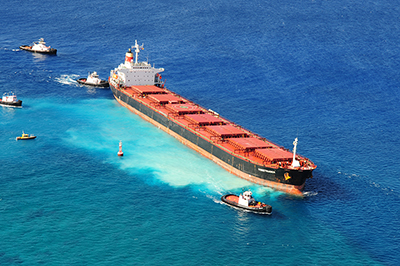 The 734-foot bulk carrier M/V VogeTrader after it ran aground near Oahu, on February 5, 2010. The milky color in the water beneath the ship is the pulverized coral. (USCG)