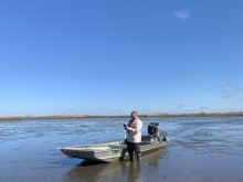 a man strands in front of a flats boat in mudflats 