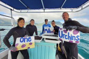 a group of adults in wetsuits stand on a boat holding signs that read one million urchins
