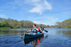 Restoration at the New Bedford Harbor Superfund site included parks and increasing access to the waterfront. Young people paddle in a canoe on calm waters. Credit: Buzzards Bay Coalition