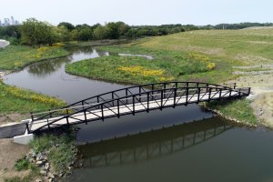 a pedestrian bridge is pictured over a small river with green grass on either side 