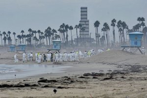 Oil spill workers in white protective gear clean oil from a sandy beach. 