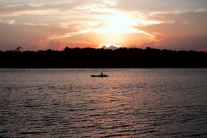 An angler on a boat on the Cape Fear River at sunset.