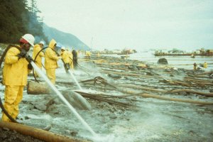 People in yellow suits hose a rocky shoreline