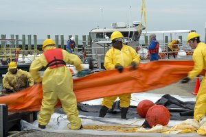 Workers in yellow protective gear haul in an orange boom at an oil spill site. 