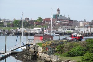 the Gloucester harbor is pictured with boats in the background and a small boathouse and ramp in the foreground